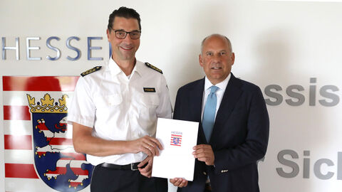 Alttext: Innenminister Roman Poseck steht Felix Paschek und überreicht ihm eine Urkunde