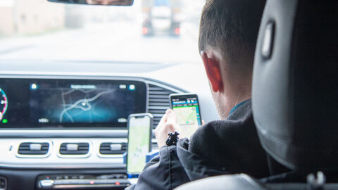 Zwei Personen in einem Fahrzeug schauen auf Smartphones mit Kartenmaterian