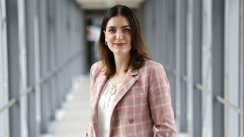 Eine Kollegin mit rosafarbenen Blouson in einem langen Glasdurchgang