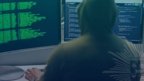 Düstere Person sitzt vor PC mit Programmiersprache auf dem Bildschirm 