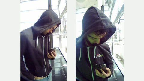 Foto des unbekannten Täters; männlicher Täter mit schwarzen Kaputzenpullover blickt auf sein Handy