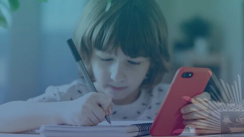 Kind sitzt mit Smartphone am Schreibtisch 