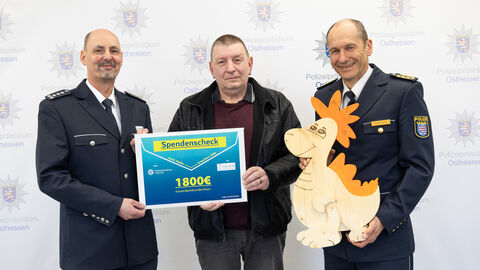 EPHK Klaus Eckert mit Herrn Schneider vom Verein Kleine Helden und Polizeipräsident Michael Tegethoff übergeben einen Spendenscheck über 1800 Euro vor einer Präsentationswand