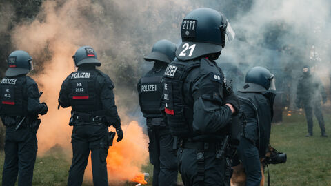 Mehrere Einsatzkräfte mit Schutzausrüstung, orangene Rauchwolke im Hintergrund 