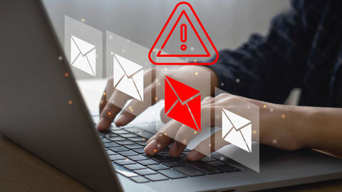 Person sitzt an Laptop, eingeblendet im Bild sind vier E-Mail-Symbole, eines davon in roter Farbe, darüber ist ein "Achtungs-Symbol" in rot eingeblendet (Ausrufezeichen im Dreieck)