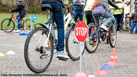 Radfahrausbildung der Jugendverkehrsschule; Das Foto zeigt mehrere Kinder, die auf Fahrrädern über einen mit Markierungen gesteckten Kurz Fahrübungen machen