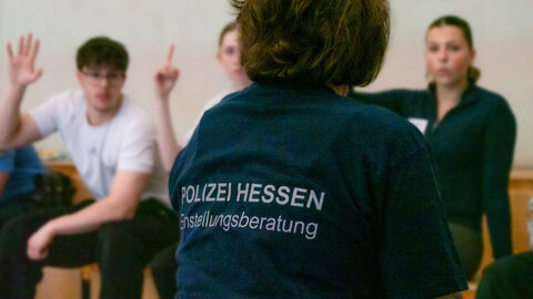 Corina Weisbrod im Gespräch mit Teilnehmenden der CopChallenge von hinten mit dunkelblauem T-Shirt. Aufdruck "POLIZEI HESSEN Einstellungsberatung" 