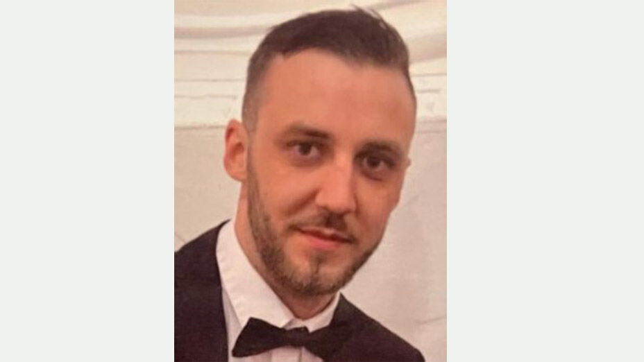 männliche Person mit dunklen Haaren und 3-Tage-Bart, hier mit weißem Hemd, schwarzem Jackettt und Fliege