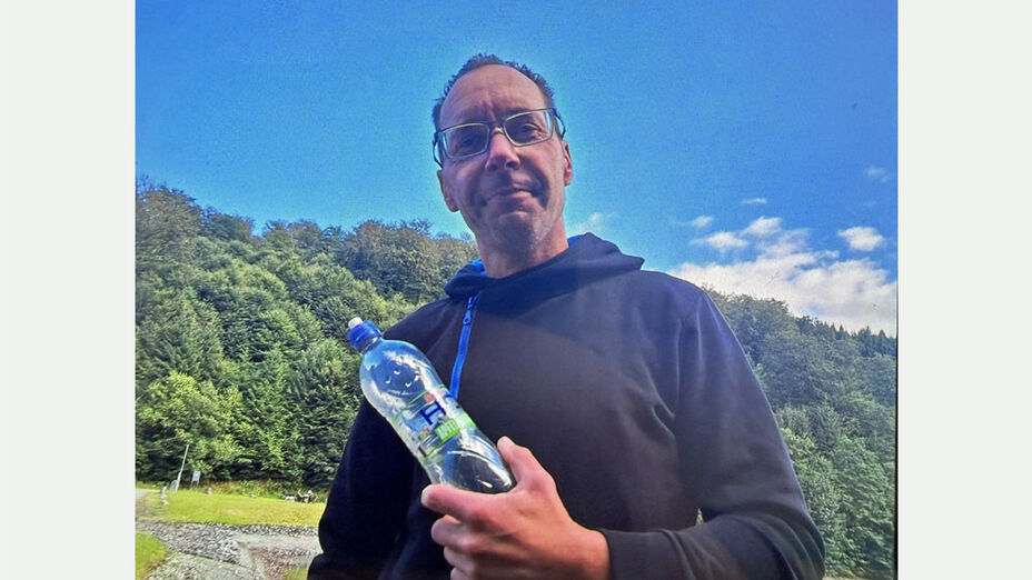 Vermisster Lars W.; Foto zeigt eine männliche Person mit Brille und kurzem Haar vor einer Waldlichtung stehend, in der Hand eine Wasserflasche